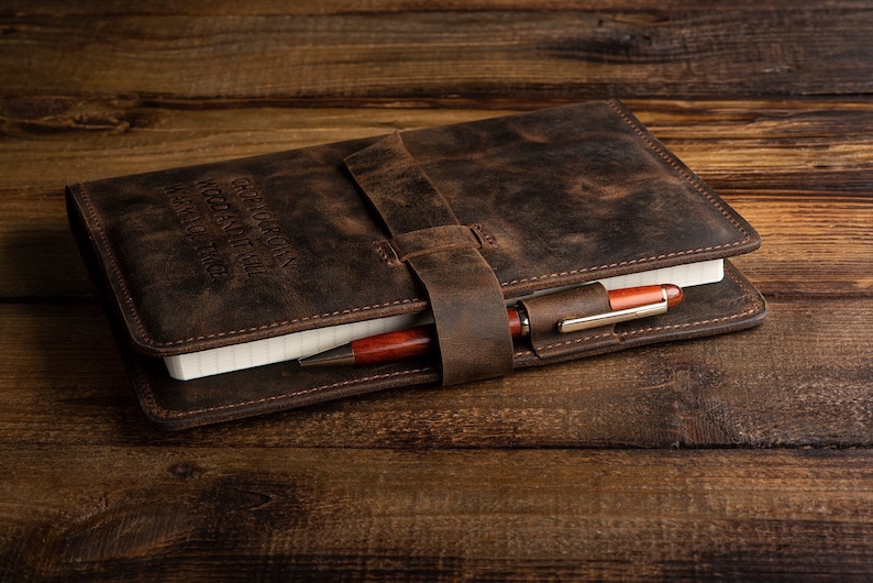 May include: A brown leather journal with a pen tucked into the strap. The journal has the words "Geography, History, Words, and Time, Learn to Trace" embossed on the cover.