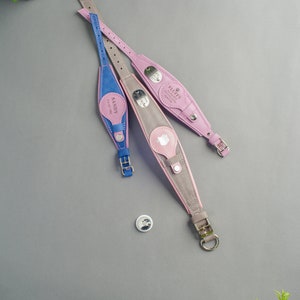 May include: Three leather dog collars in pink, grey, and blue with personalised name tags. The collars have silver buckles and D-rings. The name tags are engraved with the names "Fluffy", "Sandy", and "Max".