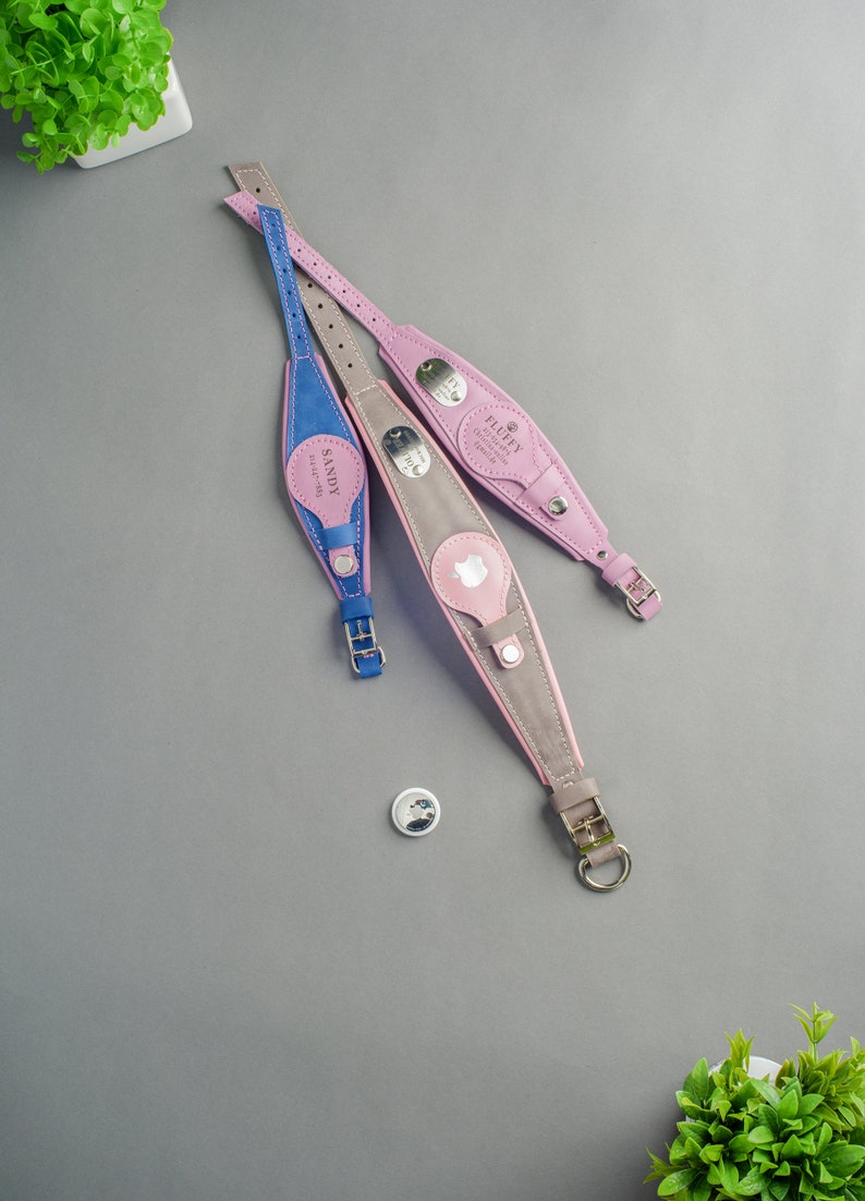 May include: Three leather dog collars in pink, grey, and blue with personalised name tags. The collars have silver buckles and D-rings. The name tags are engraved with the names "Fluffy", "Sandy", and "Max".