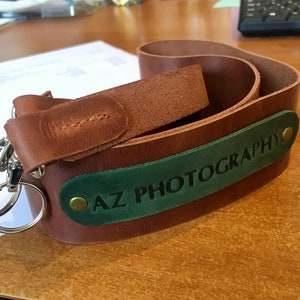 May include: A brown leather camera strap with a green leather patch that says "AZ PHOTOGRAPHY" in white lettering.