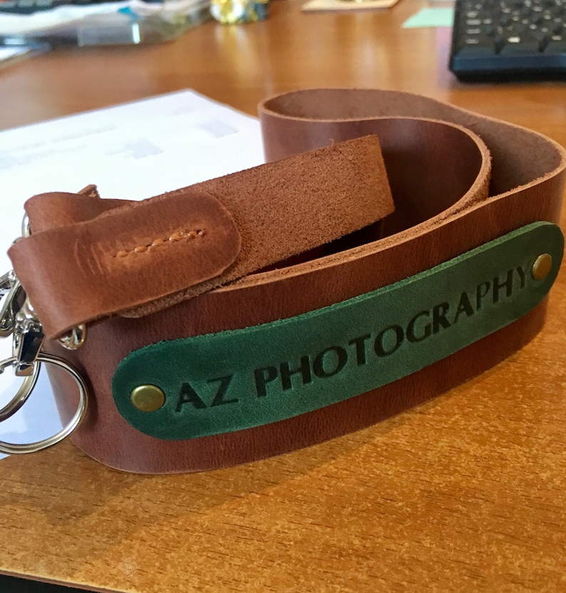 May include: A brown leather camera strap with a green leather patch that says "AZ PHOTOGRAPHY" in white lettering.