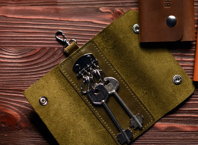 May include: A green leather key holder with a silver key ring and keys. The key holder has a flap that closes with a snap.