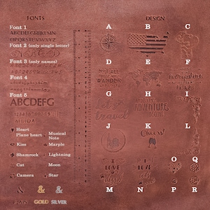 May include: A brown leather surface displays various font styles, designs, and symbols for personalization. Designs include a compass, American flag, Snoopy, world map, and phrases like "Let's travel." Also shown are hearts, stars, and paw prints.