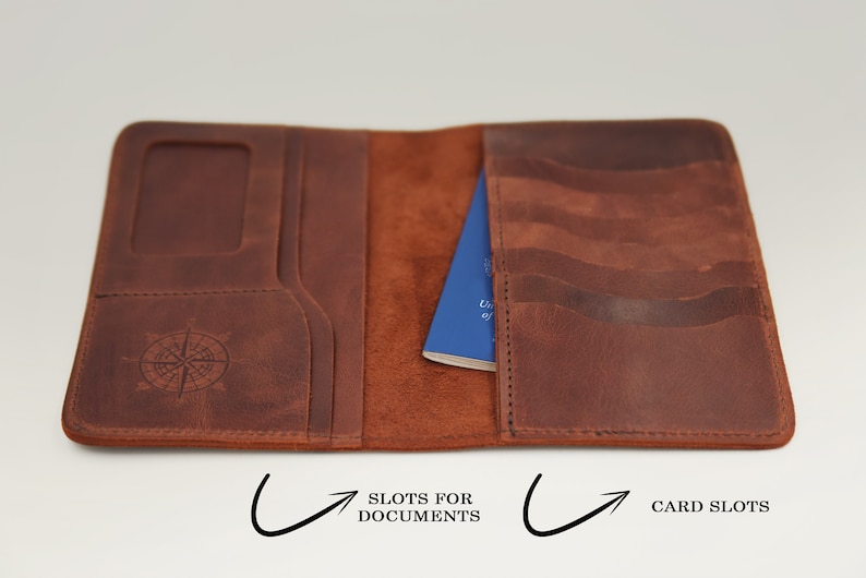 K&ouml;nnte beinhalten: Ein braunes Leder-Reisepass-Etui mit einem Kompass-Design auf der Vorderseite. Es hat F&auml;cher f&uuml;r Dokumente und Kartenf&auml;cher im Inneren.