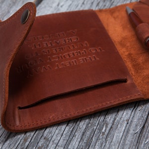 May include: A brown leather journal with a pen. The journal is open, revealing a pocket and the embossed quote: "THE BEST WAY TO PREDICT YOUR FUTURE IS TO CREATE IT. - A. LINCOLN." The pen is brown with silver accents.