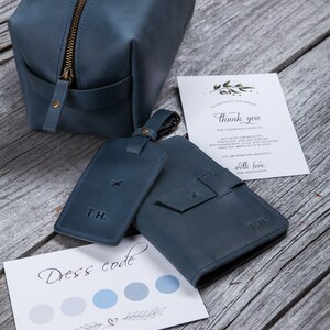Puede incluir: Un conjunto de accesorios de viaje de cuero en azul oc&eacute;ano. El conjunto incluye una bolsa de aseo, un portapasaporte y una etiqueta de equipaje. La etiqueta de equipaje tiene las iniciales "T.H." grabadas. El portapasaporte tiene un peque&ntilde;o dise&ntilde;o de avi&oacute;n grabado. La bolsa de aseo tiene una cremallera. El conjunto est&aacute; sobre una superficie de madera. La tarjeta de la imagen dice "Dress code" y tiene una paleta de colores azul y gris.
