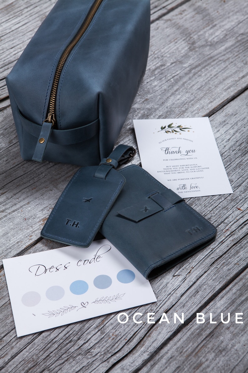 Puede incluir: Un conjunto de accesorios de viaje de cuero en azul oc&eacute;ano. El conjunto incluye una bolsa de aseo, un portapasaporte y una etiqueta de equipaje. La etiqueta de equipaje tiene las iniciales "T.H." grabadas. El portapasaporte tiene un peque&ntilde;o dise&ntilde;o de avi&oacute;n grabado. La bolsa de aseo tiene una cremallera. El conjunto est&aacute; sobre una superficie de madera. La tarjeta de la imagen dice "Dress code" y tiene una paleta de colores azul y gris.