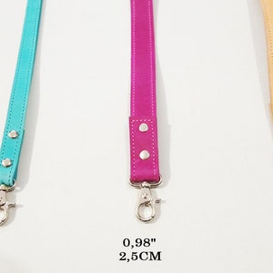 May include: Three leather straps in turquoise, fuchsia, and tan, each with a metal clasp. The turquoise strap is 0.62 inches (1.6 cm) wide, the fuchsia strap is 0.98 inches (2.5 cm) wide, and the tan strap is 1.18 inches (3 cm) wide. The text "WIDTH SIZES" is at the top.