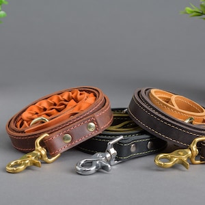 Peut inclure: Trois laisses pour chien en cuir de couleur marron, noir et beige. Les laisses sont enroulées et ont des fermoirs métalliques.