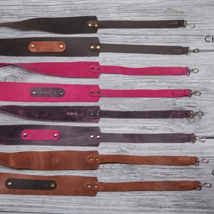 May include: Four leather camera straps in different colors: dark chocolate, pink rose, royal violet, and cognac. Each strap has a personalized nameplate.