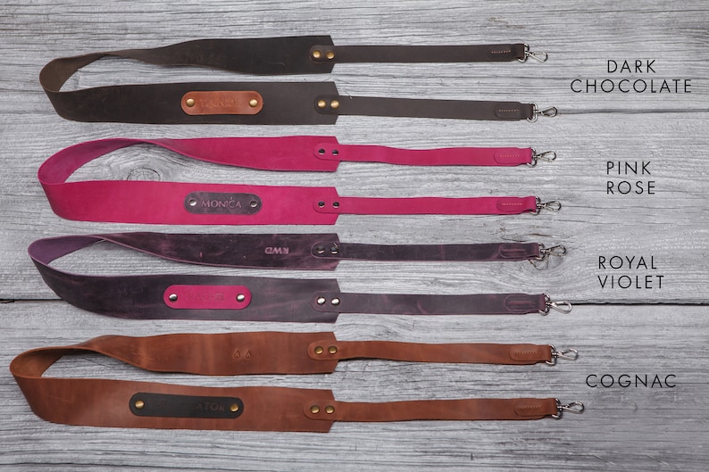May include: Four leather camera straps in different colors: dark chocolate, pink rose, royal violet, and cognac. Each strap has a personalized nameplate.