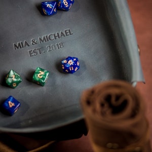 K&ouml;nnte beinhalten: Ein blaues Leder-W&uuml;rfeltablett mit der Aufschrift "MIA & MICHAEL EST. 2018" und mehreren blauen und gr&uuml;nen W&uuml;rfeln.