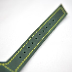 Puede incluir: Una correa de reloj de color verde oscuro con acabado mate y costuras de contraste en color amarillo brillante a lo largo de los bordes. La correa incluye una fila &uacute;nica de orificios de ajuste circulares espaciados uniformemente.