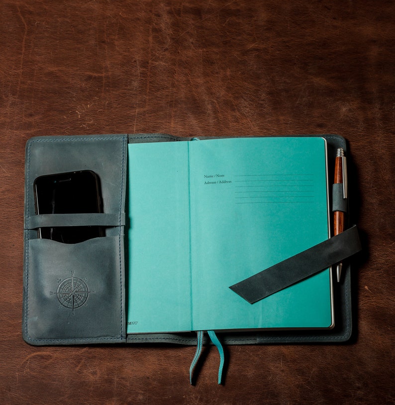 May include: A teal blue leather-bound journal with a pen and a phone holder. The journal has a section for "Name/Nom" and "Address/Adresse".