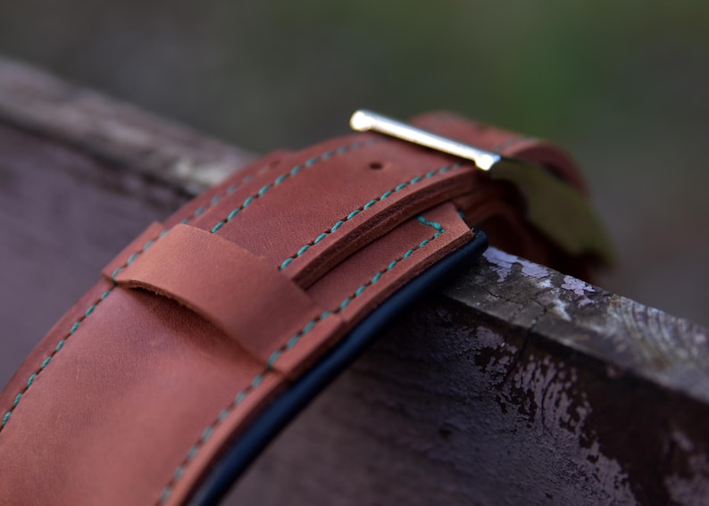 Puede incluir: Una correa de reloj de cuero color canela con costuras en contraste de color verde azulado a lo largo de los bordes. La correa incluye una trabilla de cuero y una hebilla de metal plateado pulido, con una construcci&oacute;n en capas visible.