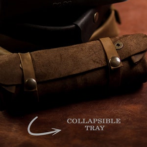 K&ouml;nnte beinhalten: Ein braunes Leder-Rolltablett mit Druckverschluss und Metall-Akzenten. Das Tablett ist mit "COLLAPSIBLE TRAY" beschriftet.