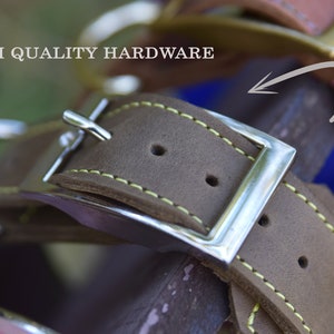 Op de afbeelding: Close-up van een bruine leren hondenriem met een zilveren gesp en gele stiksels. De tekst "HIGH QUALITY HARDWARE" is zichtbaar op de achtergrond.