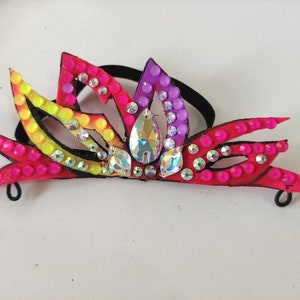 K&ouml;nnte beinhalten: Ein farbenfrohes Haarschmuckst&uuml;ck mit Blumenmuster. Das Accessoire ist aus Stoff gefertigt und hat Strasssteine. Es ist an einem schwarzen Gummiband befestigt.