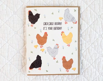Op de afbeelding: Een verjaardagskaart met een kleurrijke illustratie van kippen en kuikens. De kaart luidt "Chick, chick hooray! It's your birthday!"