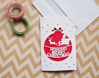 May include: A white card with a red and white paper cut-out design of a Christmas ornament with the text "HOHOHO MERRY CHRISTMAS".
