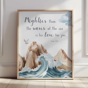 May include: A framed art print featuring an ocean scene with a large wave and rocky cliffs. The text reads "Mightier than the waves of the sea is his love for you." in elegant script. The artwork is in soft watercolor tones.