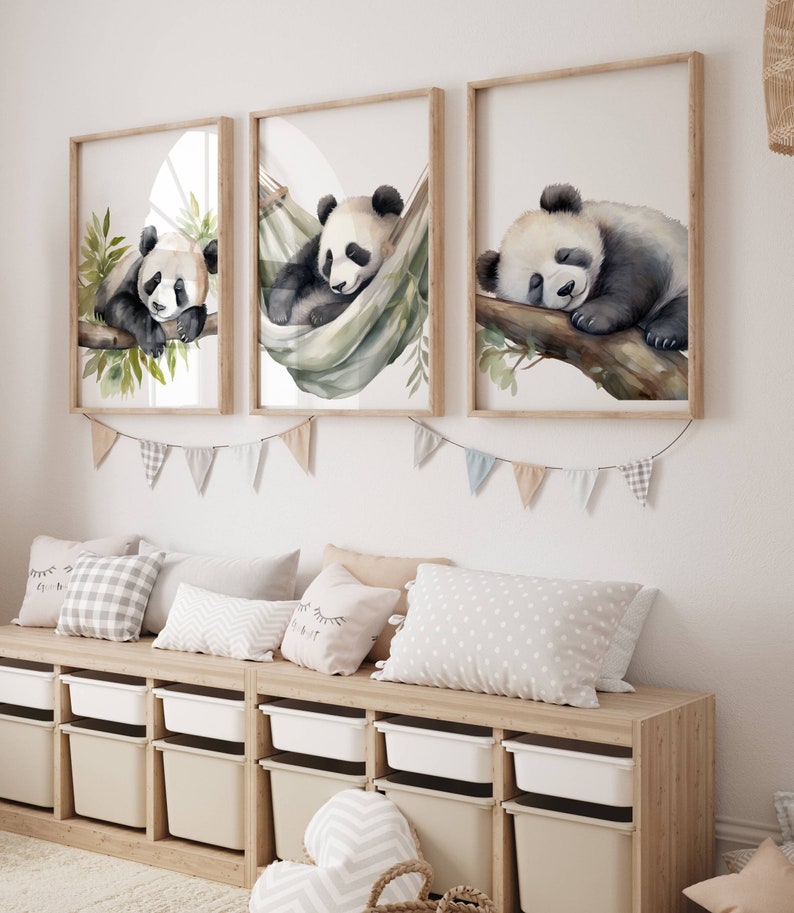 May include: Three framed watercolor prints of sleeping pandas. One panda rests on a branch, another in a hammock, and the third on a branch. The prints are above a wooden storage unit with pillows and decorative bunting.