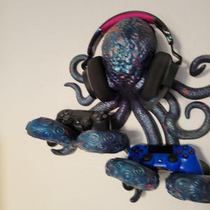 May include: A blue and purple octopus figurine with glitter accents holding a pair of black headphones and two blue video game controllers.