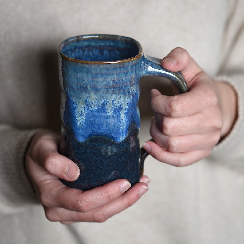 May include: A blue and black ceramic mug with a textured glaze. The mug has a wide, rounded handle.