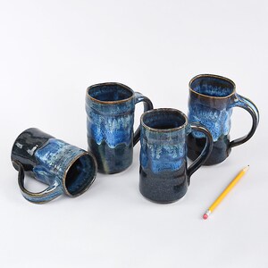 May include: Four handmade ceramic mugs with blue and black glaze. The mugs have a unique, slightly uneven shape and a handle on each side.
