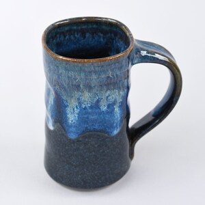 May include: A handmade ceramic mug with a blue and black glaze. The mug has a rounded body and a large handle.