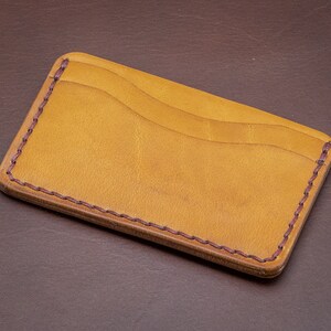 Może przedstawiać: Brązowy sk&oacute;rzany portfel ze szwem bordowym wok&oacute;ł krawędzi. Portfel ma dwa sloty na karty.