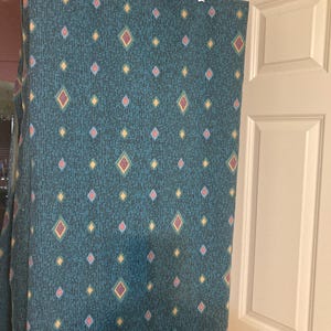 May include: A teal fabric panel featuring a repeating pattern of small diamonds in yellow, pink, and blue, set against a dark vertical textured line background. The fabric is suspended from a clear plastic hanger with silver metal clips.