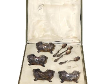 Puede incluir: Un juego de servir de plata antiguo, que incluye cuatro cuencos decorativos y cuatro cucharas, presentado en una caja verde con un forro de satén blanco. Los cuencos tienen diseños curvos ornamentados. Las cucharas tienen mangos detallados.