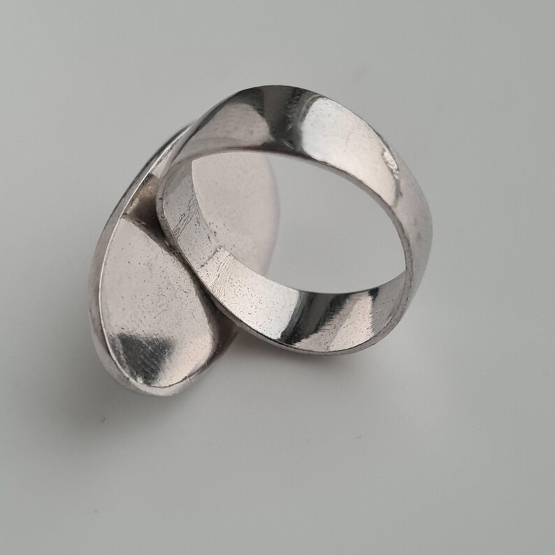 K&ouml;nnte beinhalten: Ein silberfarbener Ring mit einem einzigartigen, flie&szlig;enden Design. Der Ring hat eine durchgehende, M&ouml;biusband-&auml;hnliche Form mit einer glatten, reflektierenden Oberfl&auml;che. Das Design ist modern und abstrakt, geeignet f&uuml;r den Alltag oder besondere Anl&auml;sse.