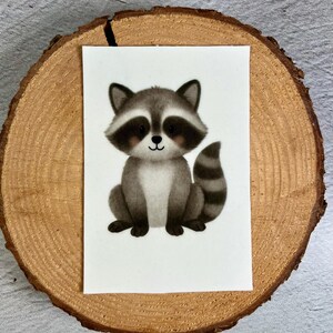Könnte beinhalten: Aquarell-Illustration eines sitzenden Waschbären. Der Waschbär hat graues Fell, eine schwarze Maske um die Augen und einen gestreiften Schwanz. Das Bild befindet sich auf weißem Hintergrund.