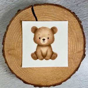 Könnte beinhalten: Aquarell-Illustration eines braunen Teddybären, der auf weißem Hintergrund sitzt. Der Bär hat einen niedlichen Ausdruck mit rosigen Wangen und ist auf einer Holzscheibe platziert.