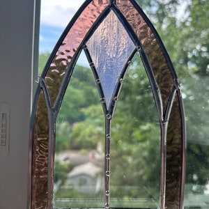 May include: A stained glass window with a pink and blue design. The window is framed in black metal and has a pointed arch shape.