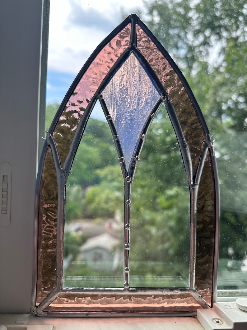 May include: A stained glass window with a pink and blue design. The window is framed in black metal and has a pointed arch shape.