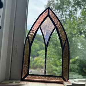 May include: A stained glass window with a pink and white design. The window is in the shape of an arch and has a black frame.