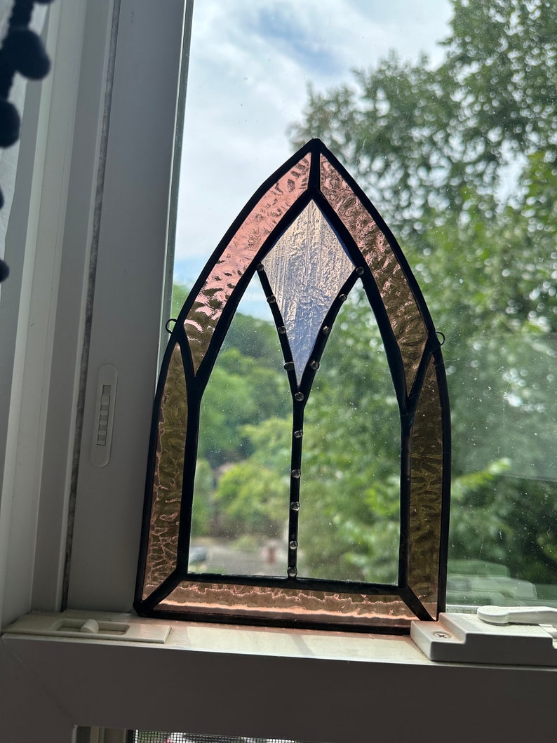 May include: A stained glass window with a pink and white design. The window is in the shape of an arch and has a black frame.