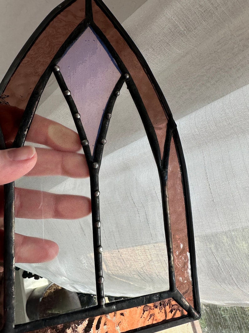 May include: A stained glass window panel with a gothic arch design. The panel features a purple glass center with a diamond shape and a copper foil border.