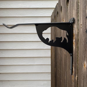 May include: Black metal bracket with a buffalo silhouette design, mounted on a wooden fence.