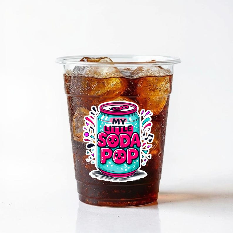 May include: A clear plastic cup filled with a dark brown beverage and ice cubes. A sticker on the cup features a cartoon soda can design with the text "MY LITTLE SODA POP" in a playful font, surrounded by colorful accents.
