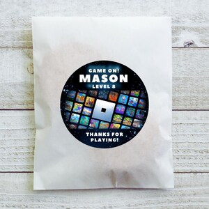 May include: A white paper bag with a circular sticker featuring the text "GAME ON! MASON LEVEL 8" in white. The sticker has a black background with a grid of colorful game images and the words "THANKS FOR PLAYING!"