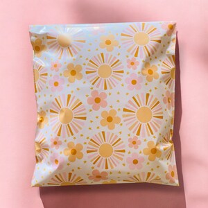 May include: A white poly mailer with a repeating pattern of pink and orange flowers and gold stars.
