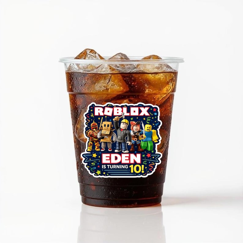 May include: A clear plastic cup filled with a dark brown beverage and ice cubes. A colorful sticker featuring Roblox characters and the text "EDEN IS TURNING 10!" is affixed to the cup, suitable for a birthday celebration.