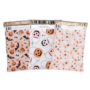 May include: Three pink and white patterned mailing envelopes with gold foil accents. The envelopes feature Halloween themes with images of pumpkins, ghosts, and bats. The text on the envelopes reads "#SmileMailPlus by Hallmark".