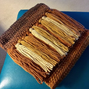 May include: A brown and cream crocheted throw blanket with long fringe tassels.