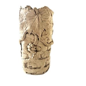 May include: A beige, textured vase with a grape leaf and grape cluster design. The vase is cylindrical and has a rough, stone-like appearance. The grape leaf and grapes are raised from the surface, adding dimension to the piece. The vase is likely made of ceramic or a similar material.