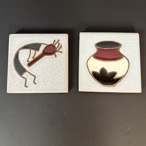Può includere: Due piastrelle quadrate in ceramica con disegni del sud-ovest. Una piastrella presenta una figura di Kokopelli in nero, grigio e rosso. L'altra piastrella mostra un vaso stilizzato in nero, rosso e crema. Entrambe le piastrelle hanno una finitura craquelé.